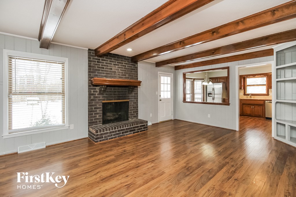 an empty living room with a brick fireplace and wooden floors
