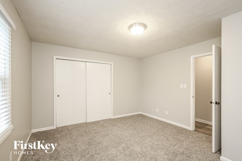 a bedroom with white walls and carpet and a door to a closet