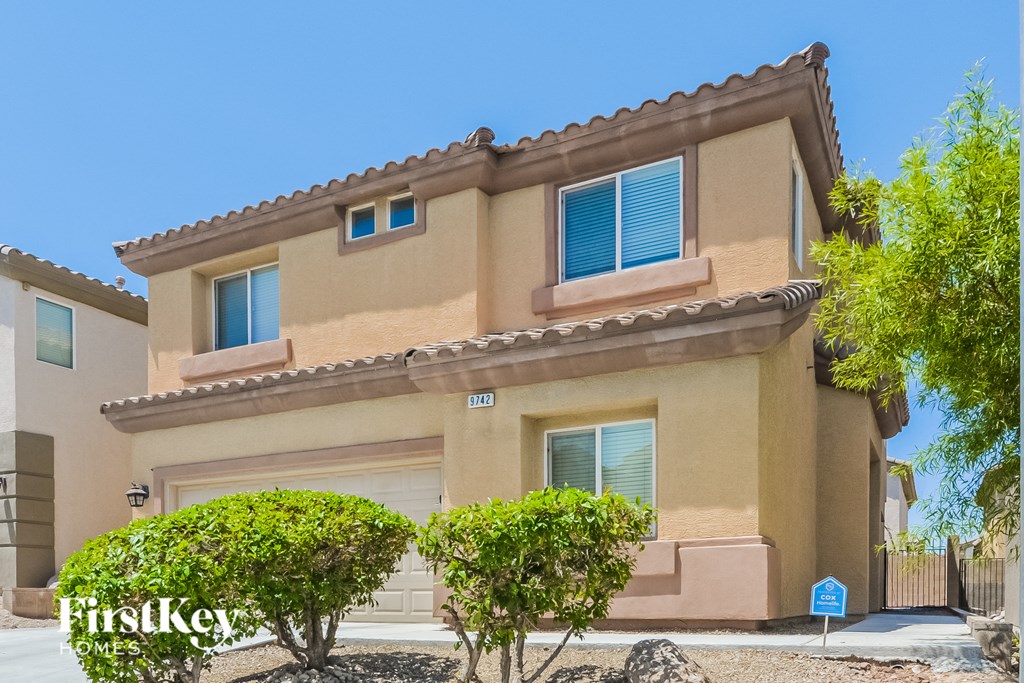 A beige stucco house with a brown roof and a blue sign in front.