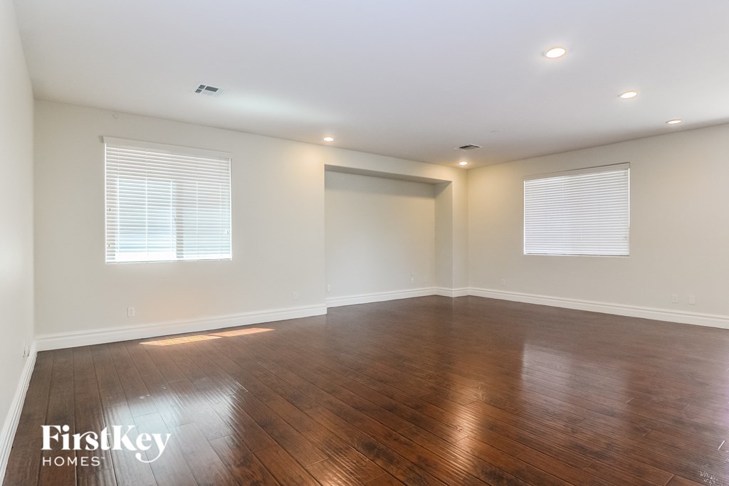 A spacious room with wooden floors and two windows with blinds.