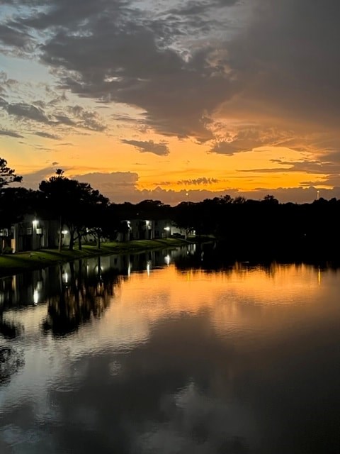 A serene lake reflects the sunset sky and the lights from the surrounding buildings.