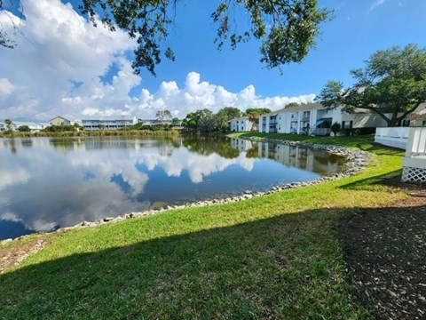 A serene lake surrounded by houses and trees under a partly cloudy sky.