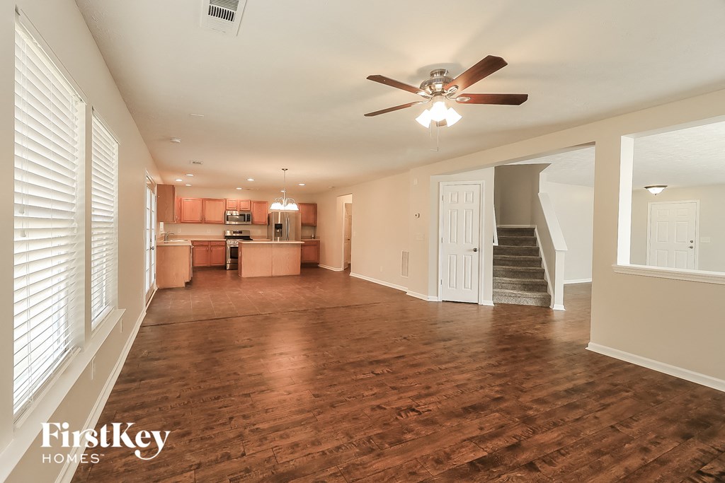 an empty living room with a ceiling fan and a kitchen