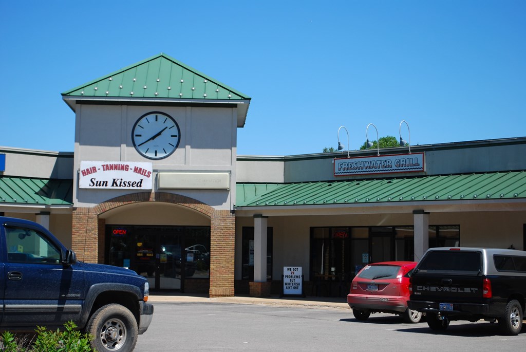 a clock on the front of a store with cars parked in front