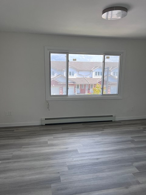an empty living room with a large window and wooden floors