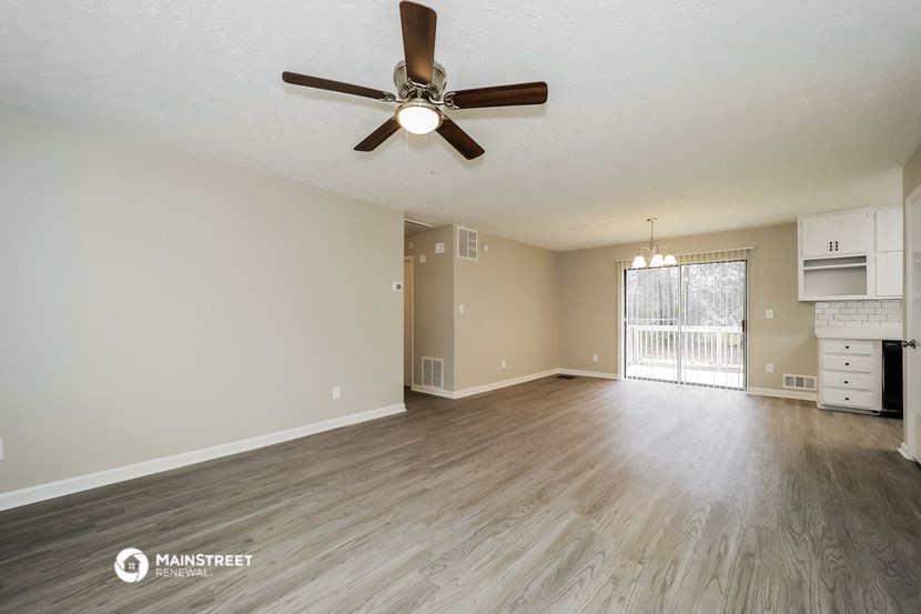 an empty living room with a ceiling fan and a kitchen