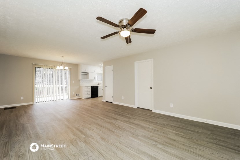 an empty living room with a ceiling fan and a kitchen