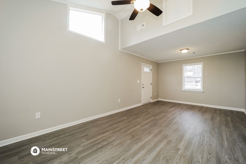 the spacious living room with hardwood floors and a ceiling fan