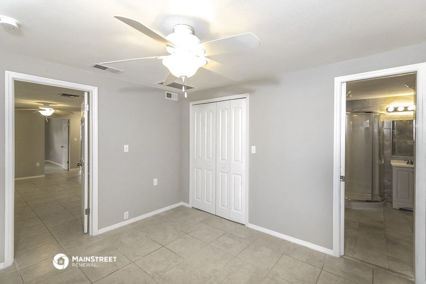 an empty living room with a ceiling fan and a door to a bathroom