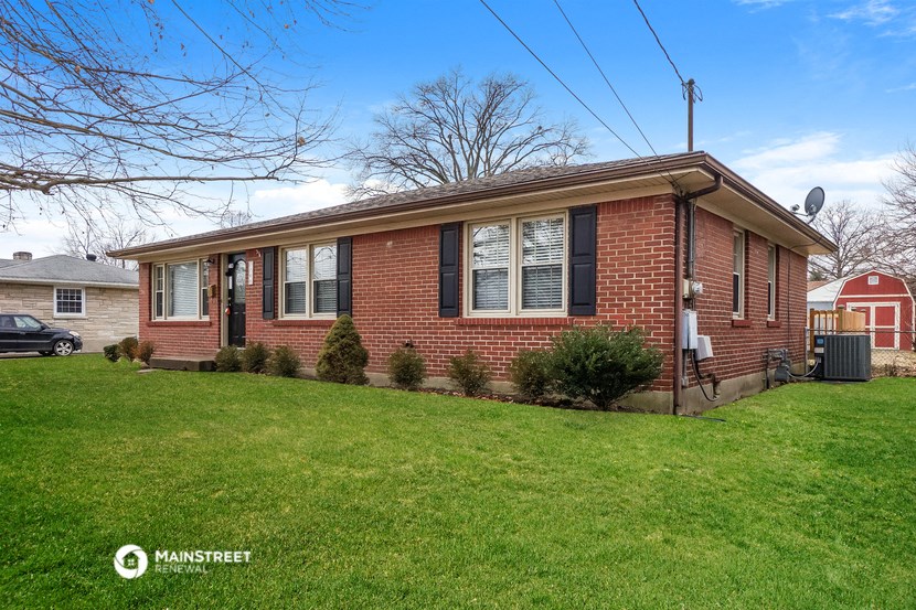 a brick house with a green lawn and a red house behind it