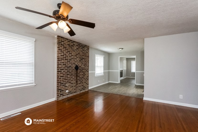an empty living room with a ceiling fan and a brick wall