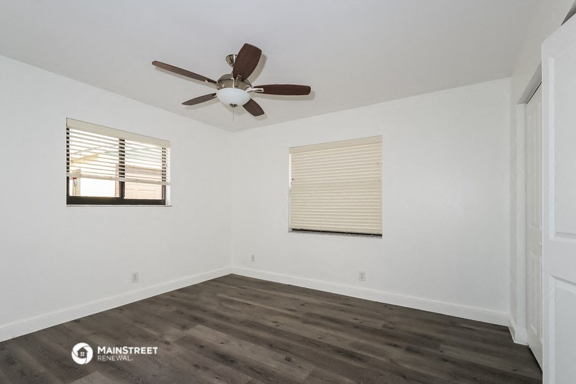 a bedroom with white walls and wood floors and a ceiling fan