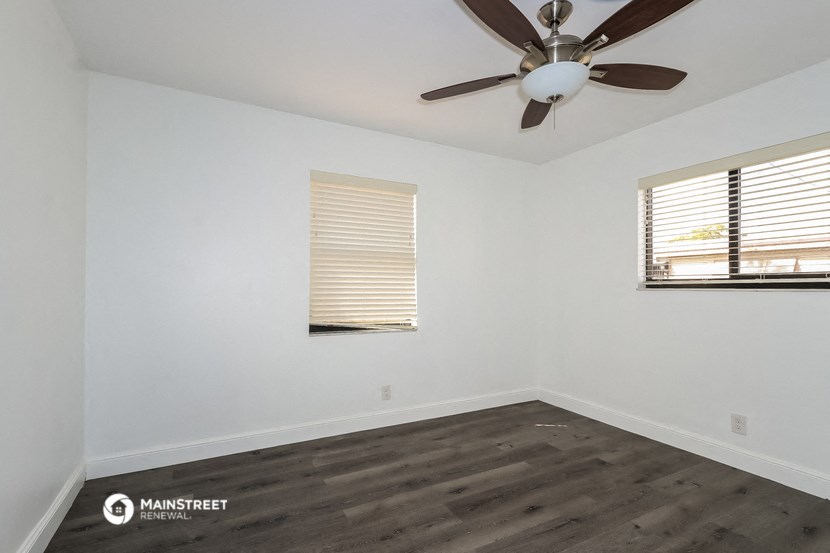 a bedroom with white walls and wood floors and a ceiling fan