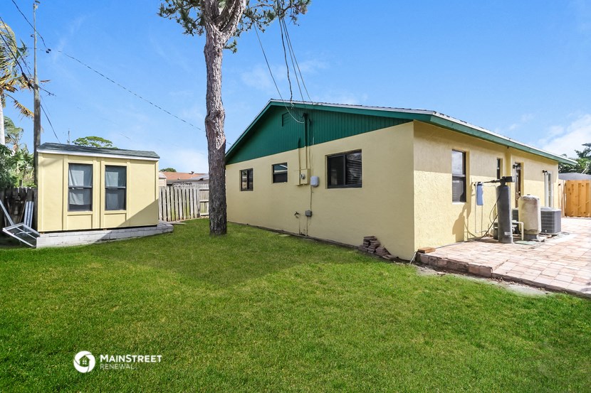 a small yellow house with a green roof and a backyard