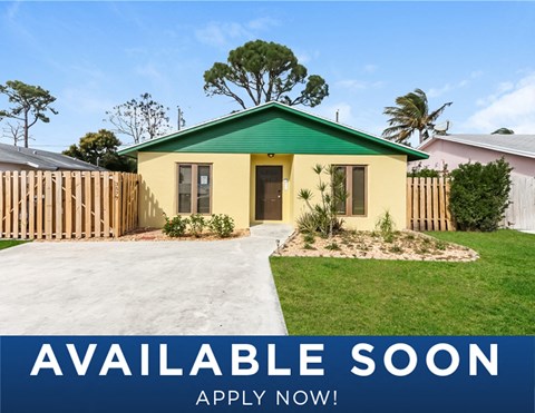 a small yellow house with a green roof and a white fence