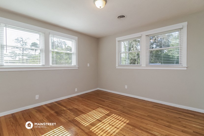 the living room of a house with wood floors and three windows