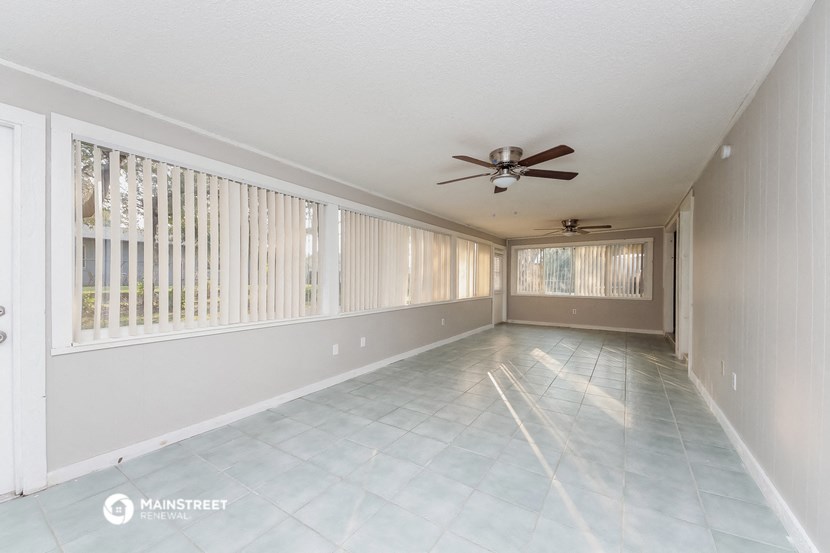 an empty living room with a ceiling fan and windows
