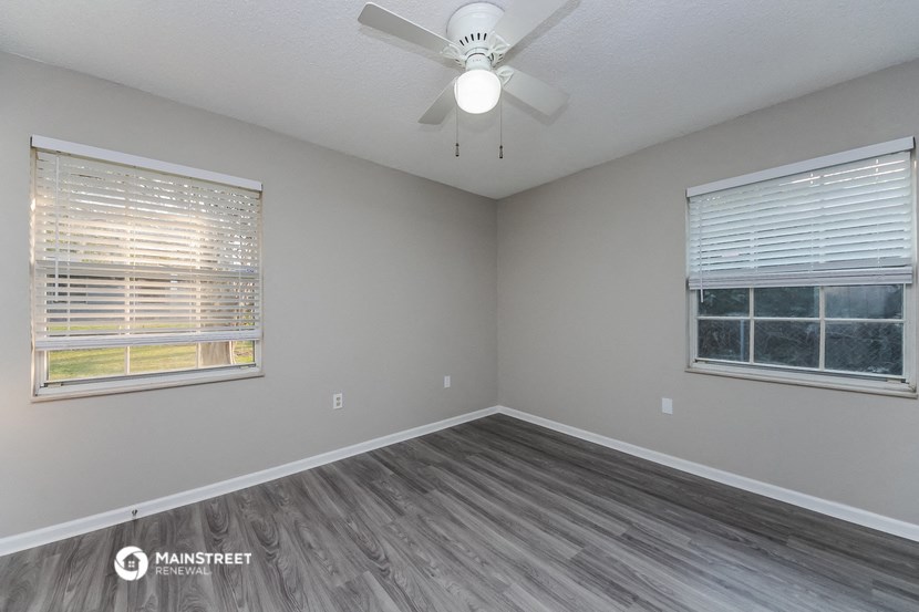 the living room of an empty house with a ceiling fan and two windows