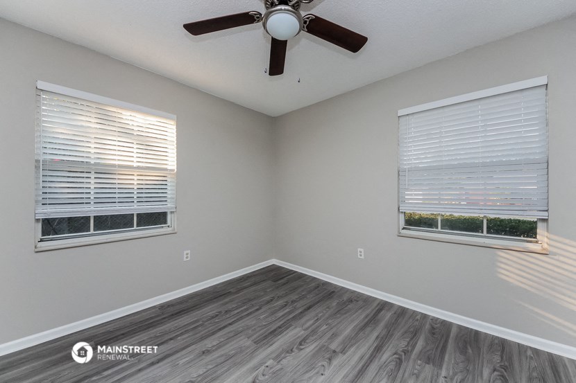 the spacious living room with two windows and a ceiling fan