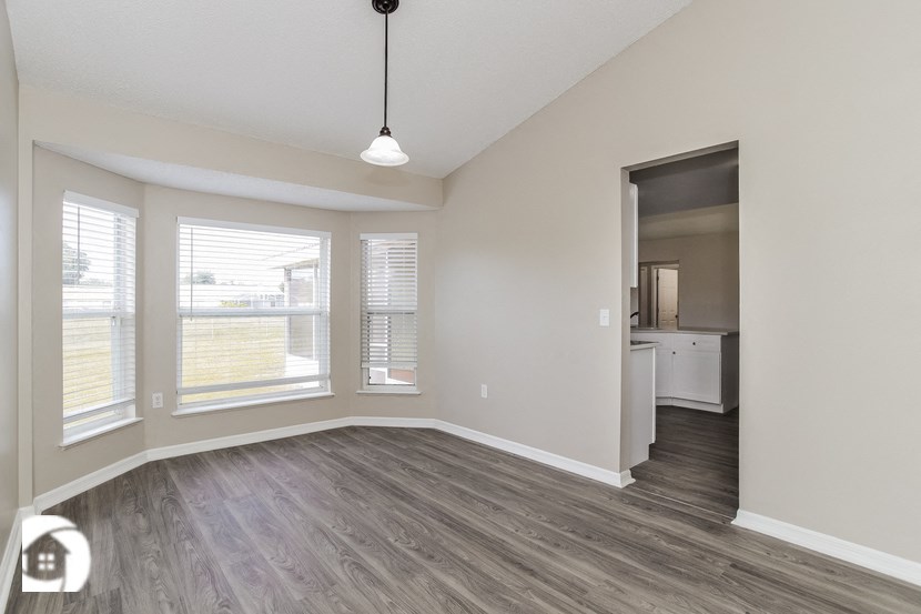 the spacious living room of an apartment with wood flooring and windows