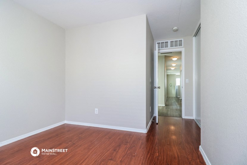 the living room and hallway of an apartment with wood flooring and white walls