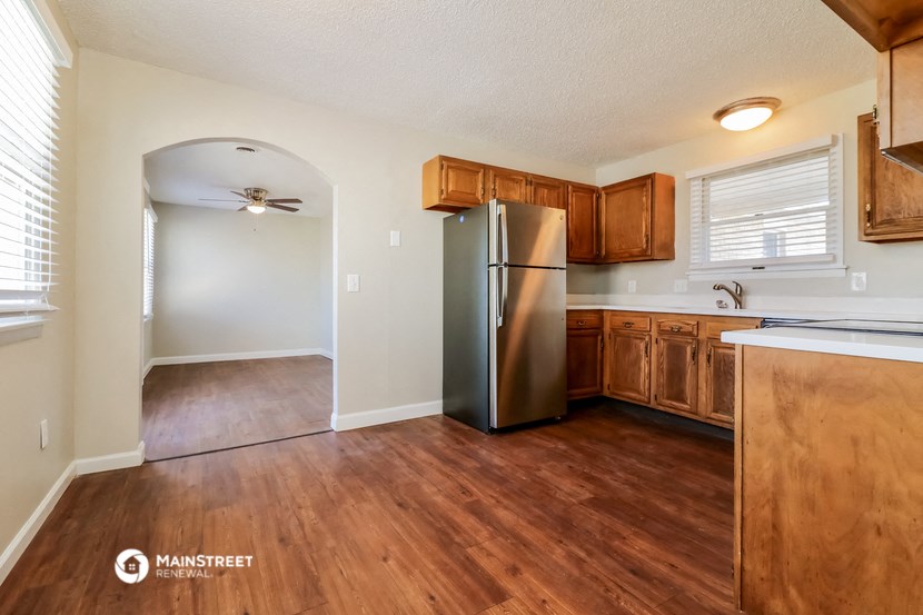 an empty kitchen with wood flooring and a stainless steel refrigerator