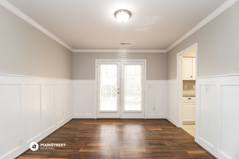 an empty living room with white walls and a door to a kitchen