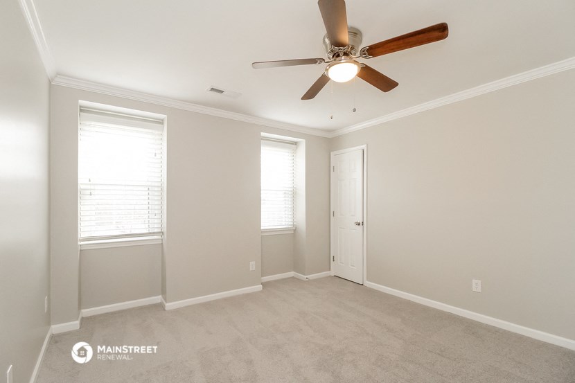 an empty room with a ceiling fan and two windows