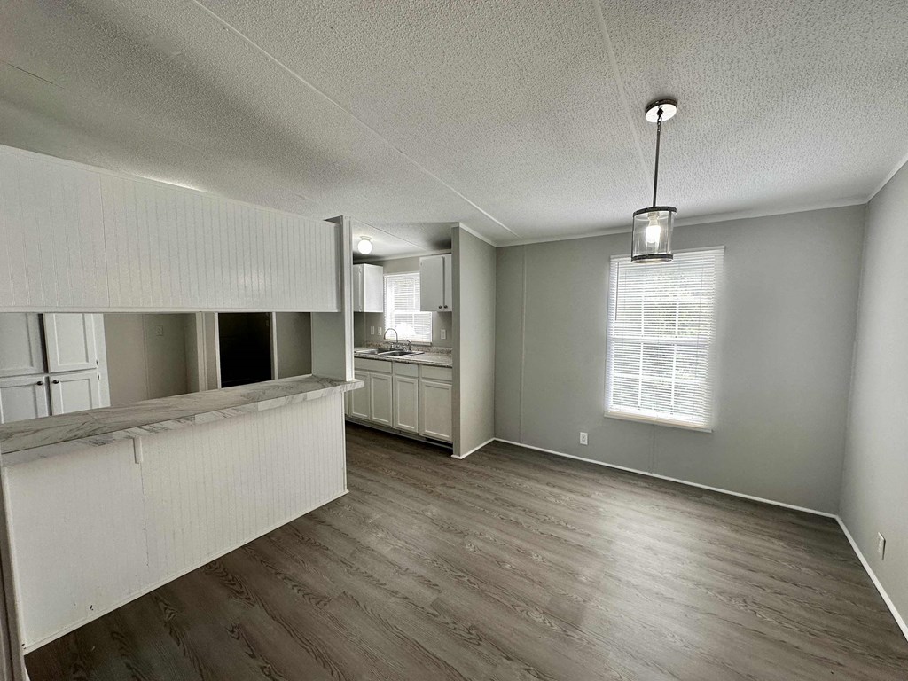 an empty living room with a kitchen and a window