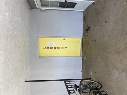 A yellow sign with black text and symbols is on a wall.