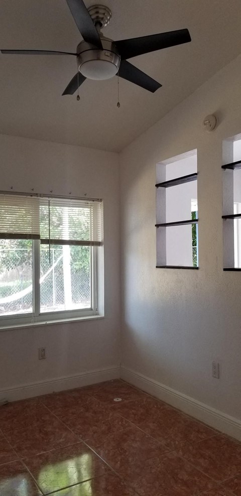 an empty living room with a ceiling fan and two windows