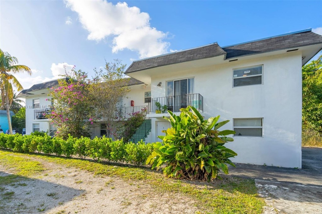 A white house with a balcony and a green lawn in front.