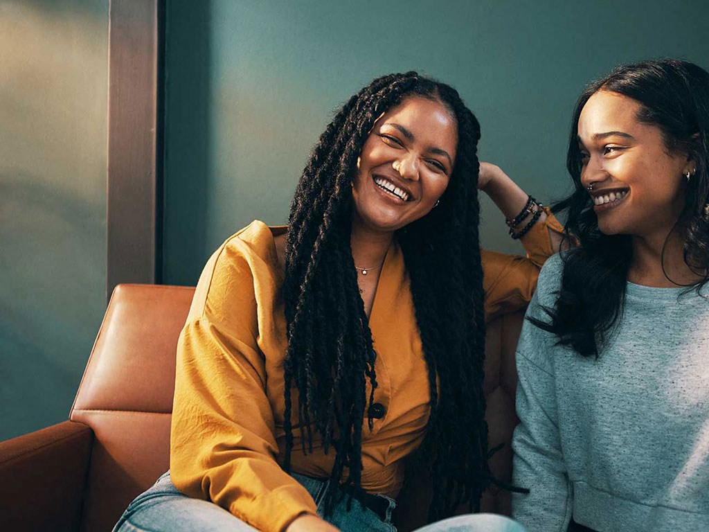 two women sitting on a couch and smiling at each other