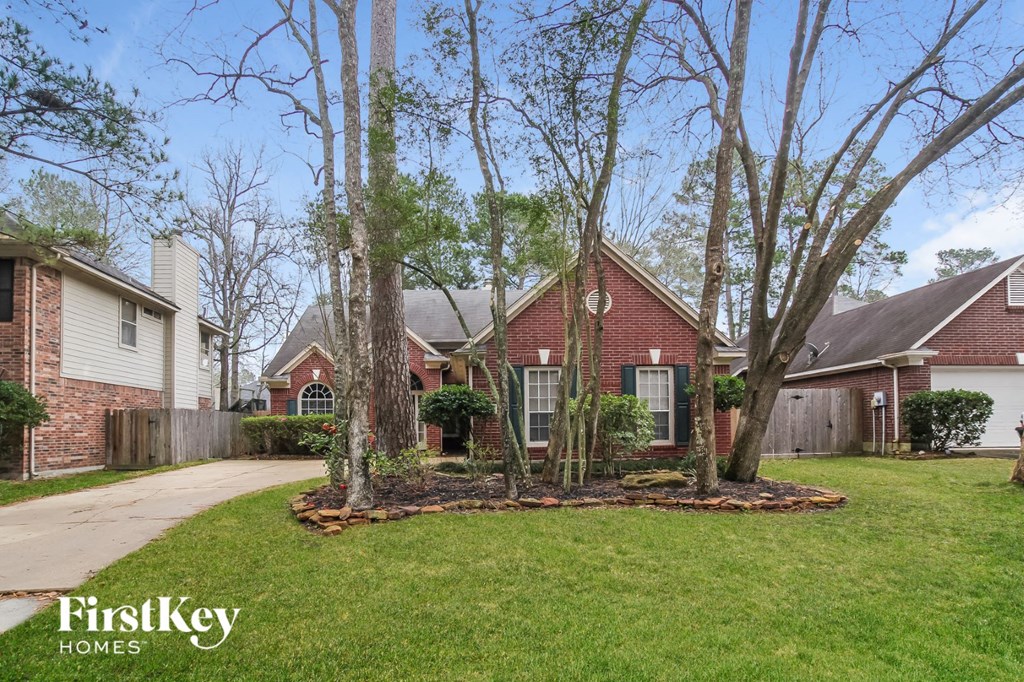 A house with a red brick facade is surrounded by a well-kept lawn and trees.