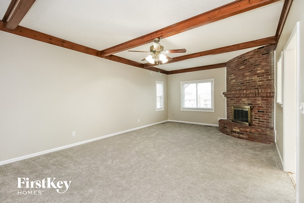 an empty living room with a brick fireplace and a ceiling fan