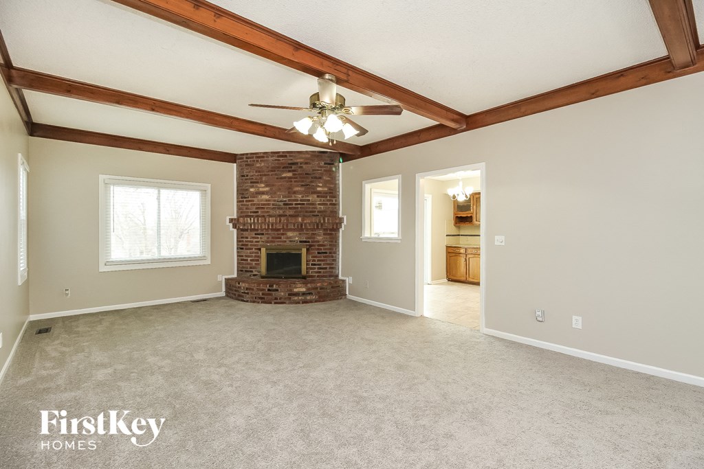 an empty living room with a brick fireplace and a ceiling fan