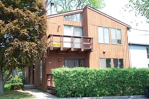 A wooden house with a balcony and a hedge in front.