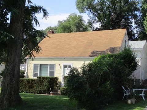 A house with a brown roof is surrounded by greenery.