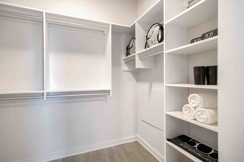 a walk in closet with white walls and shelves and a window