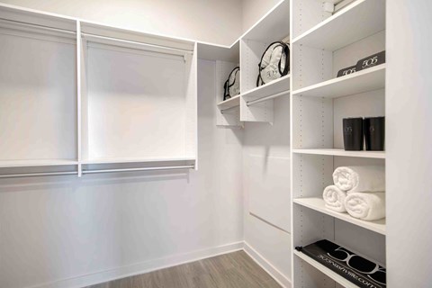 a walk in closet with white walls and shelves and a window