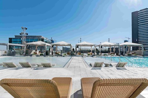 a pool with chairs and umbrellas at a hotel with tall buildings