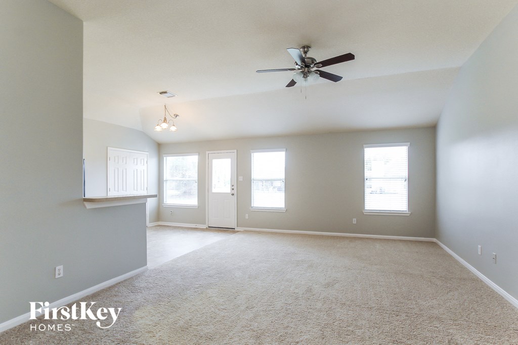 an empty living room with a ceiling fan and white carpet