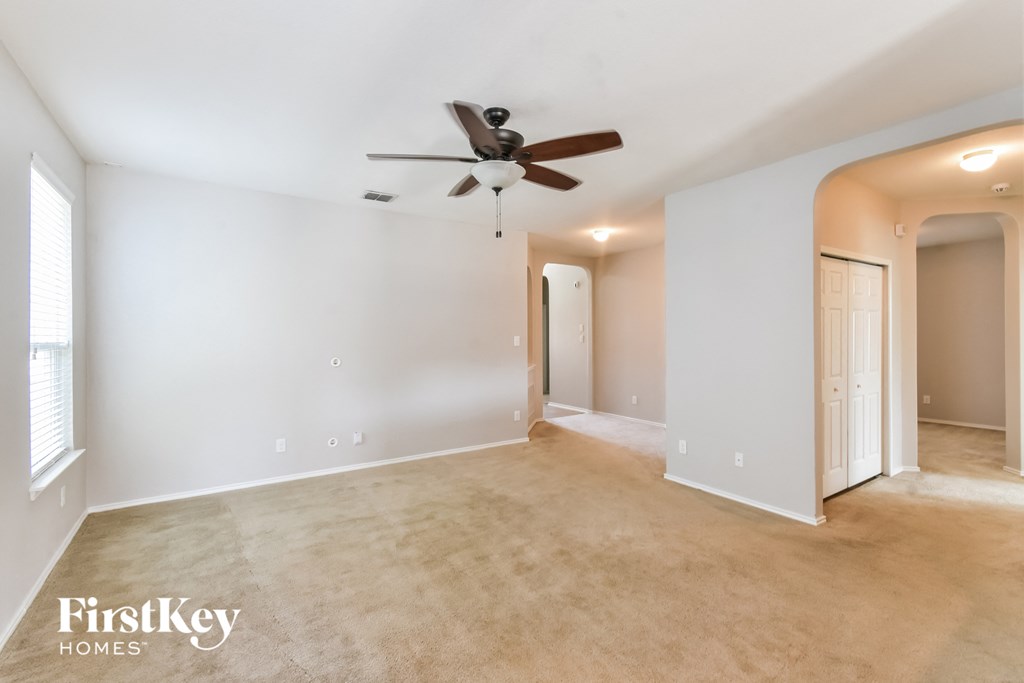 a empty living room with a ceiling fan and a door to a hallway