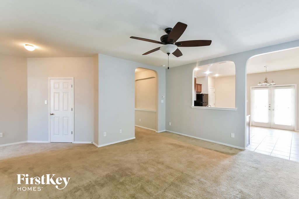 an empty living room with a ceiling fan and a door to the kitchen