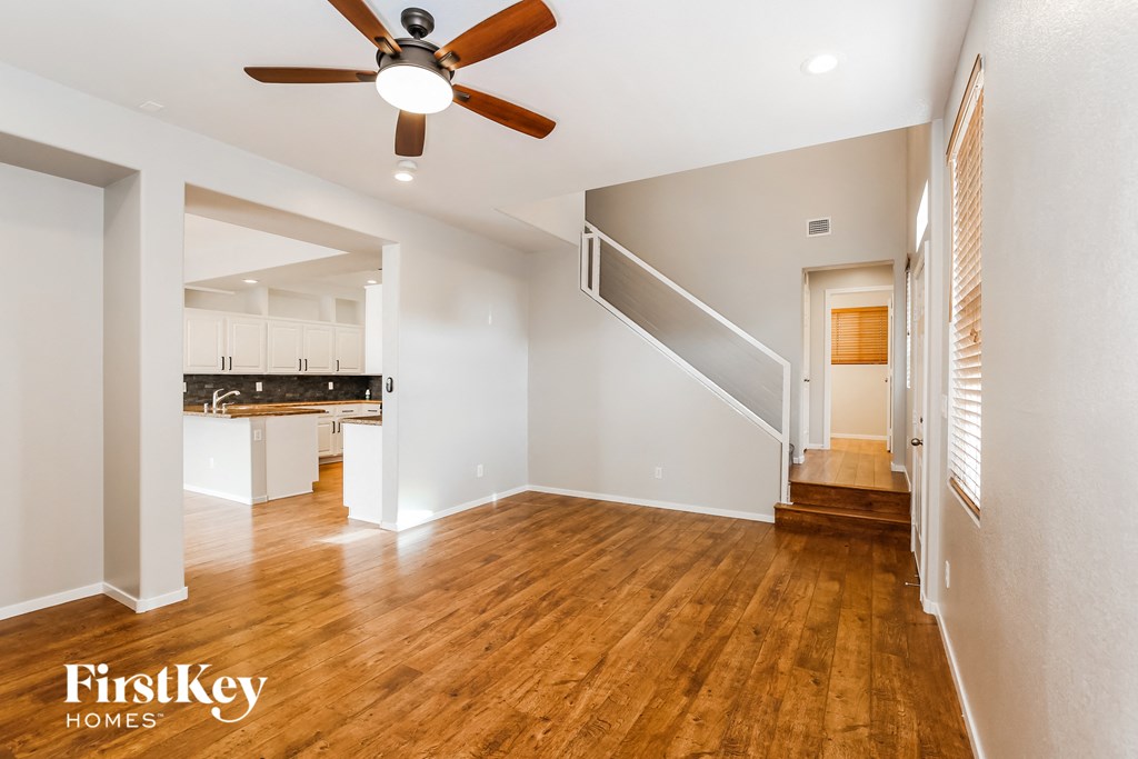 an empty living room with a ceiling fan and a kitchen