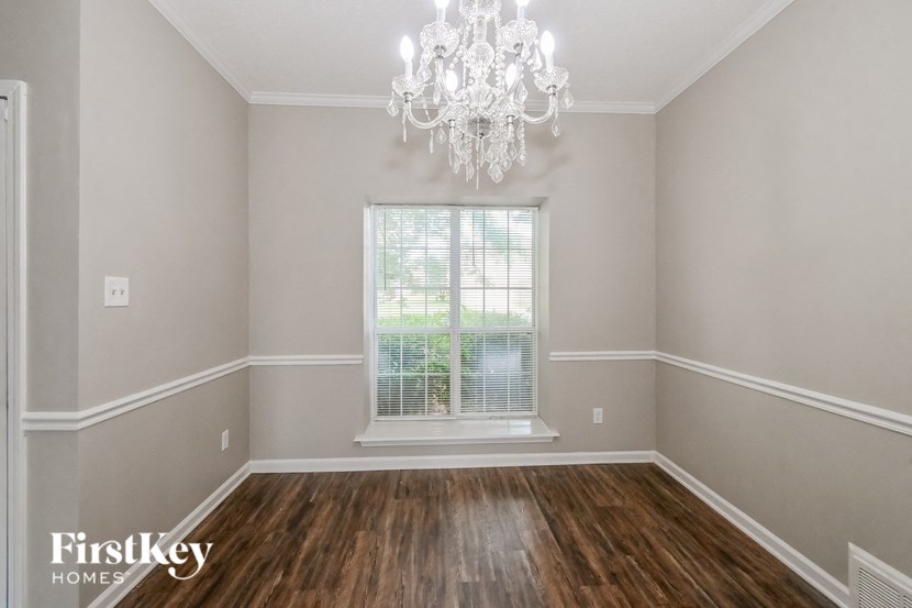 A room with a chandelier, a window with blinds, and wooden flooring.