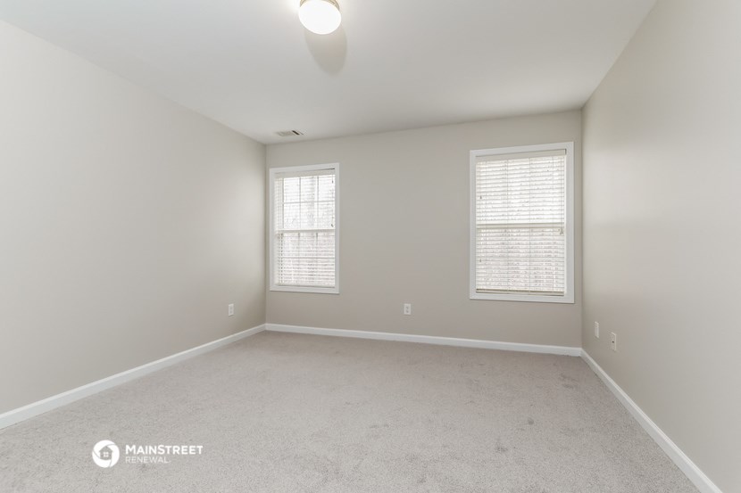 the spacious living room with two windows and carpeting