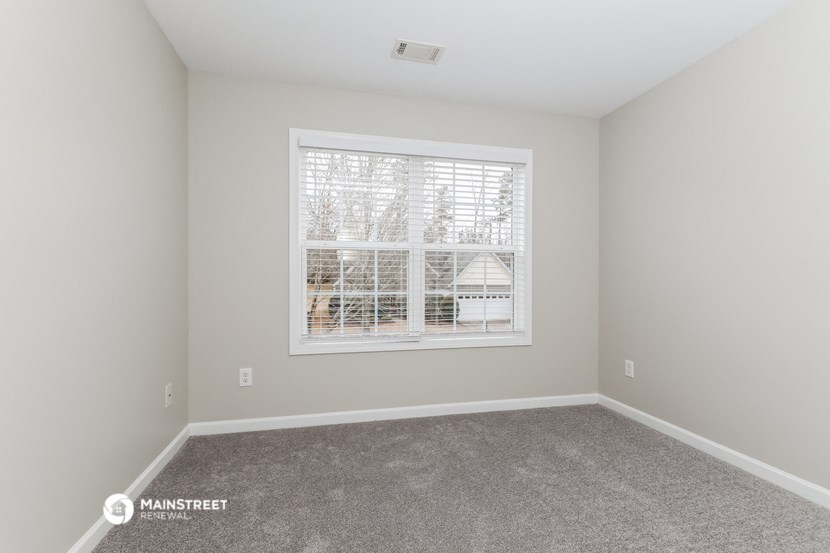 a spacious living room with a large window and carpet