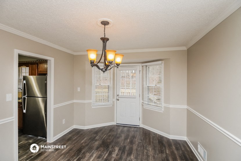 an empty living room with a refrigerator and a door to a kitchen