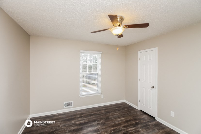the spacious living room with a ceiling fan and a white door